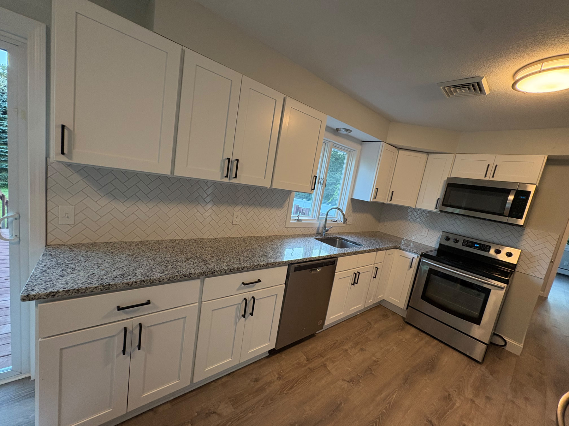 White painted kitchen cabinets with granite countertops and herringbone tile backsplash